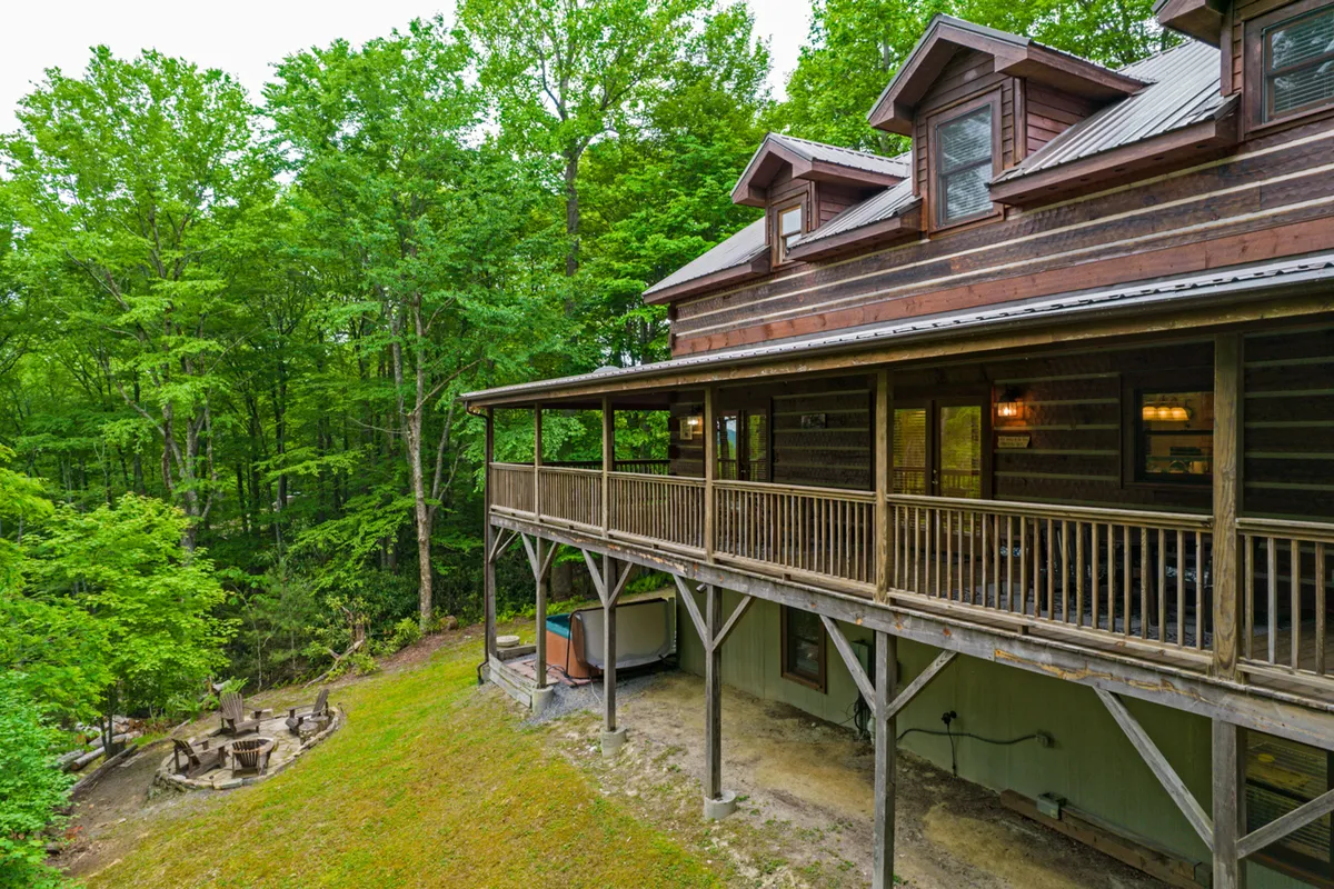 A wooden deck with a dedicated fire pit area, surrounded by trees. Multiple chairs are arranged around the fire pit, creating a cozy atmosphere for gatherings under the stars.