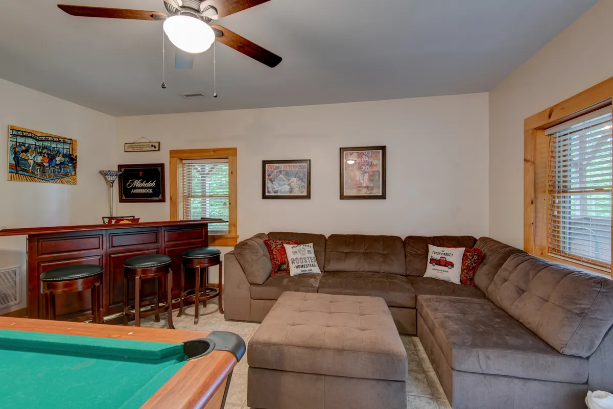 The image showcases a dedicated game room with a pool table, a bar area, a comfortable couch, and decorative wall art. The arrangement of the furniture encourages group activities and relaxation, perfectly capturing the spirit of tournament nights, friendly competitions, and movie marathons described in the section.