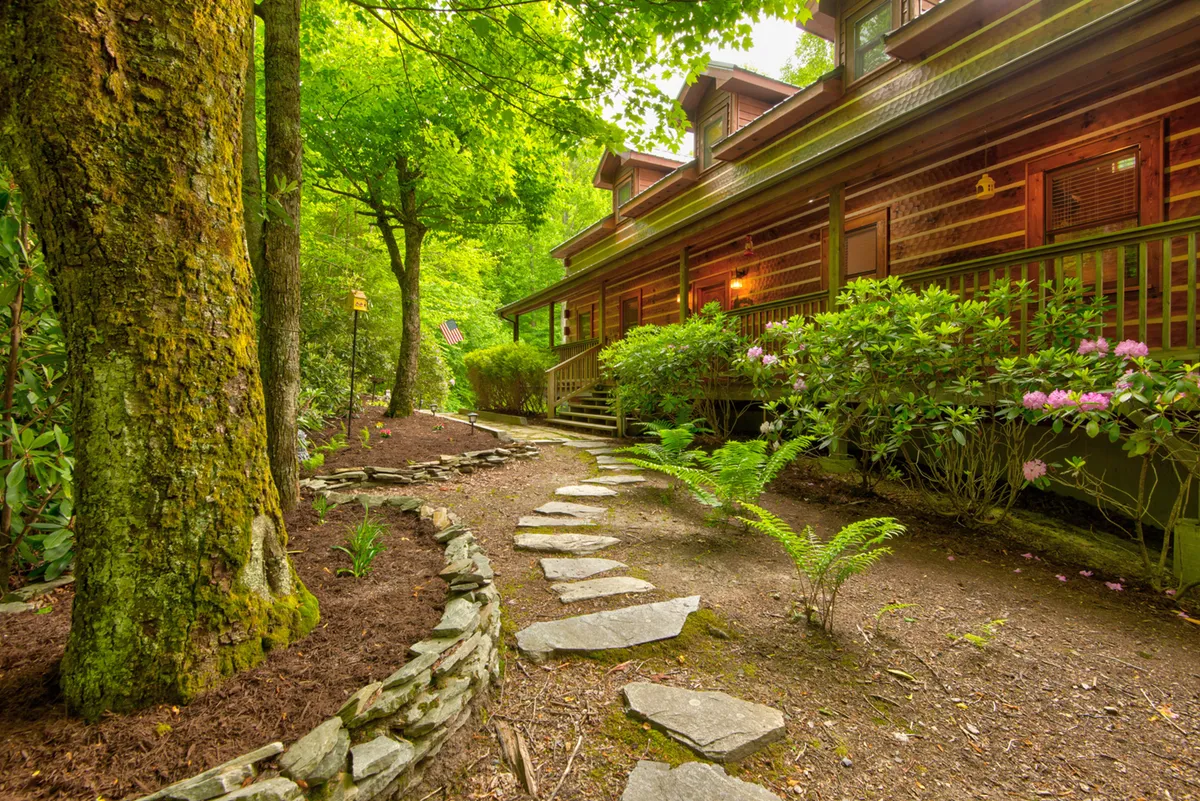 Shows a stone pathway winding through lush greenery, with the wooden facade of the house and flowering bushes in view, inviting guests to explore the natural surroundings right outside.